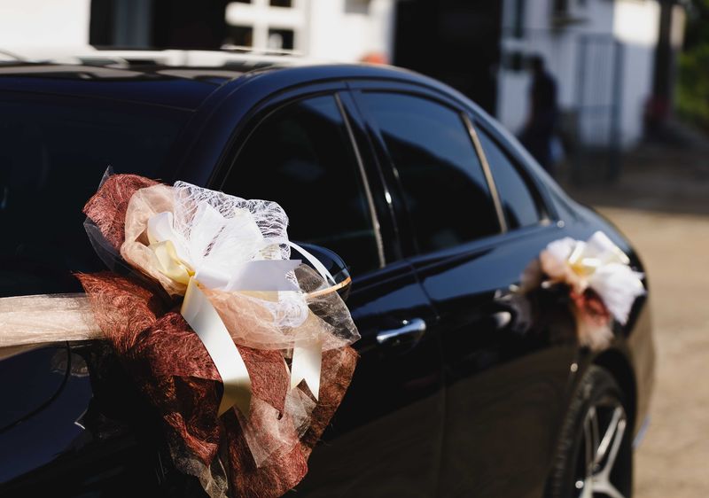 Black car decorated with ivory and bronze wedding ribbons on its doors